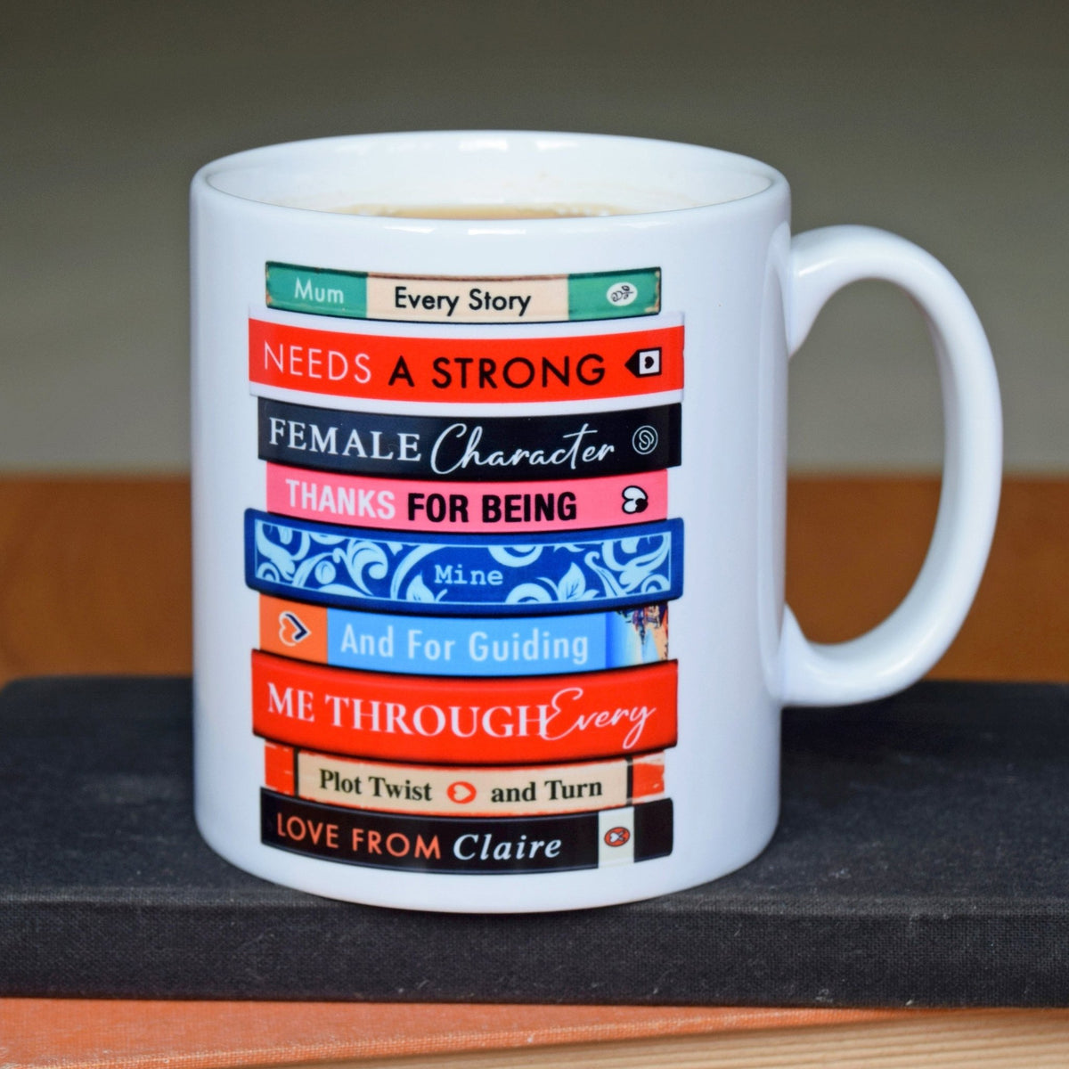 White mug with colorful book design and text on a dark surface
