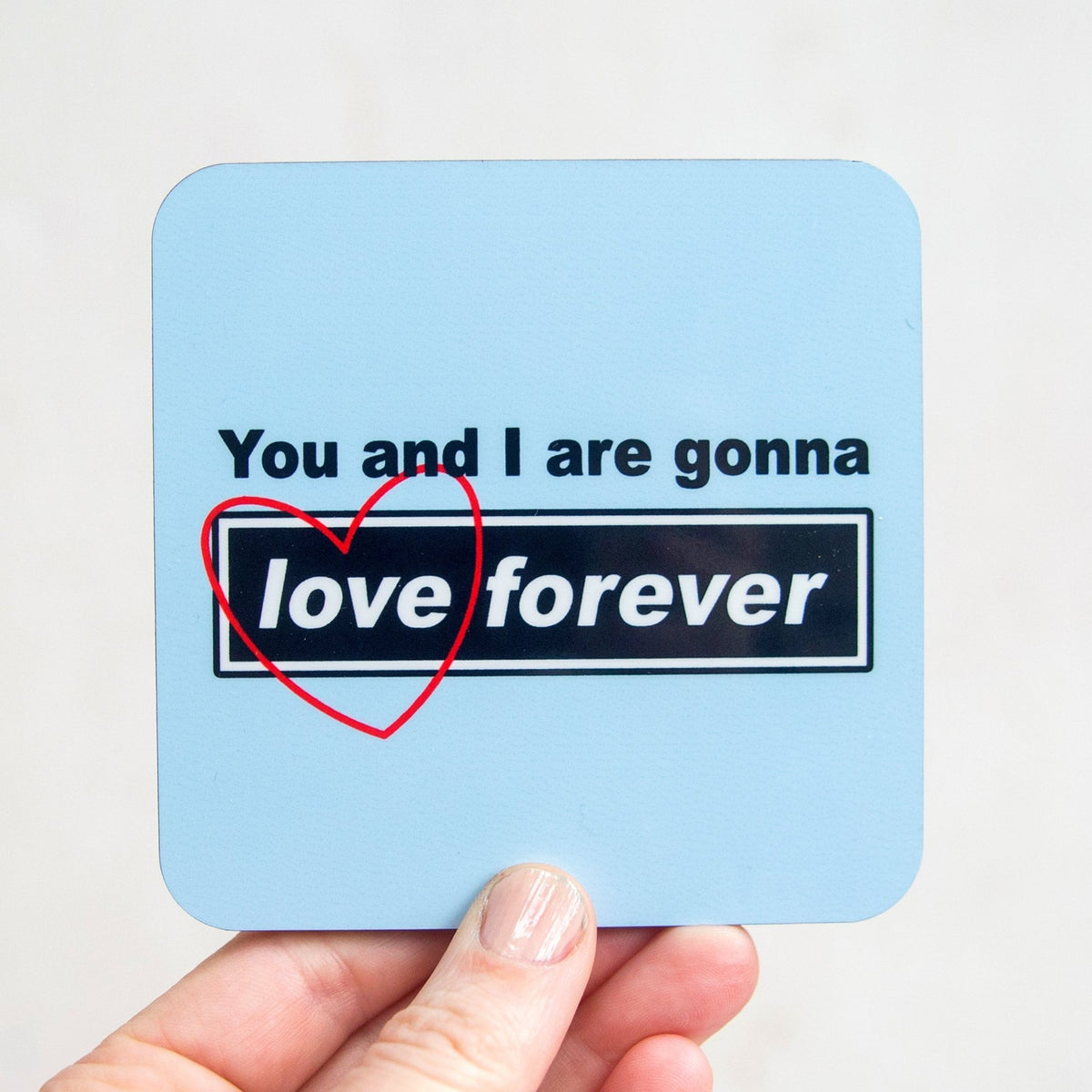 Coaster with 'You and I are gonna love forever' text on a light blue background, held by a hand.
