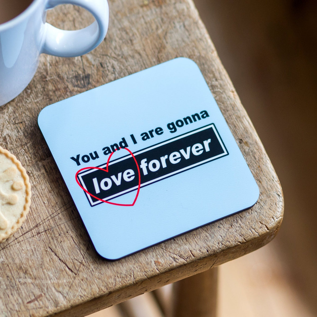 Coaster with 'You and I are gonna love forever' text on a wooden surface with a cup and cookie.