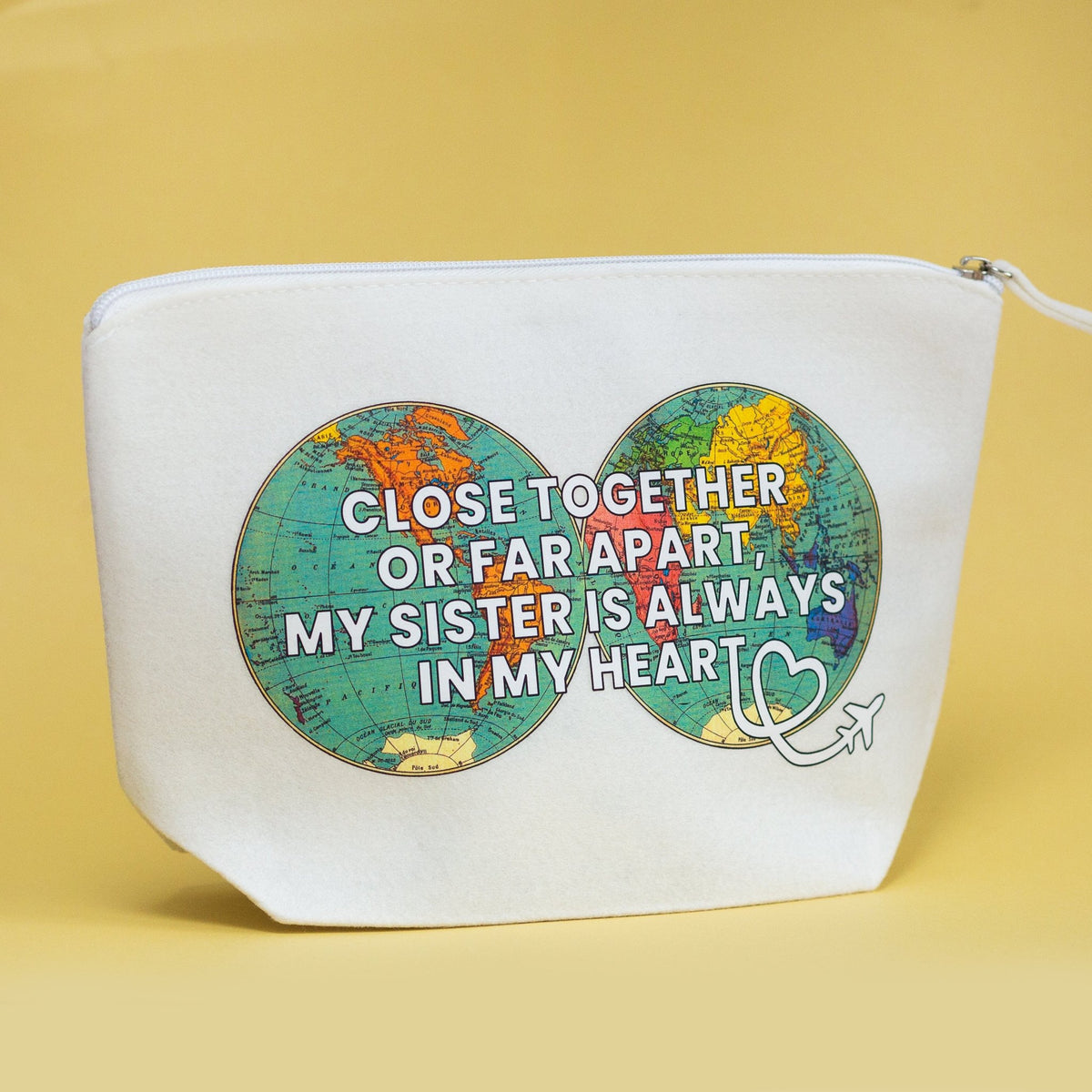 A white zippered pouch featuring a graphic of two colorful world maps forming a infinity symbol, with the text 'CLOSE TOGETHER OR FAR APART, MY SISTER IS ALWAYS IN MY HEART' and a small white heart with an airplane.