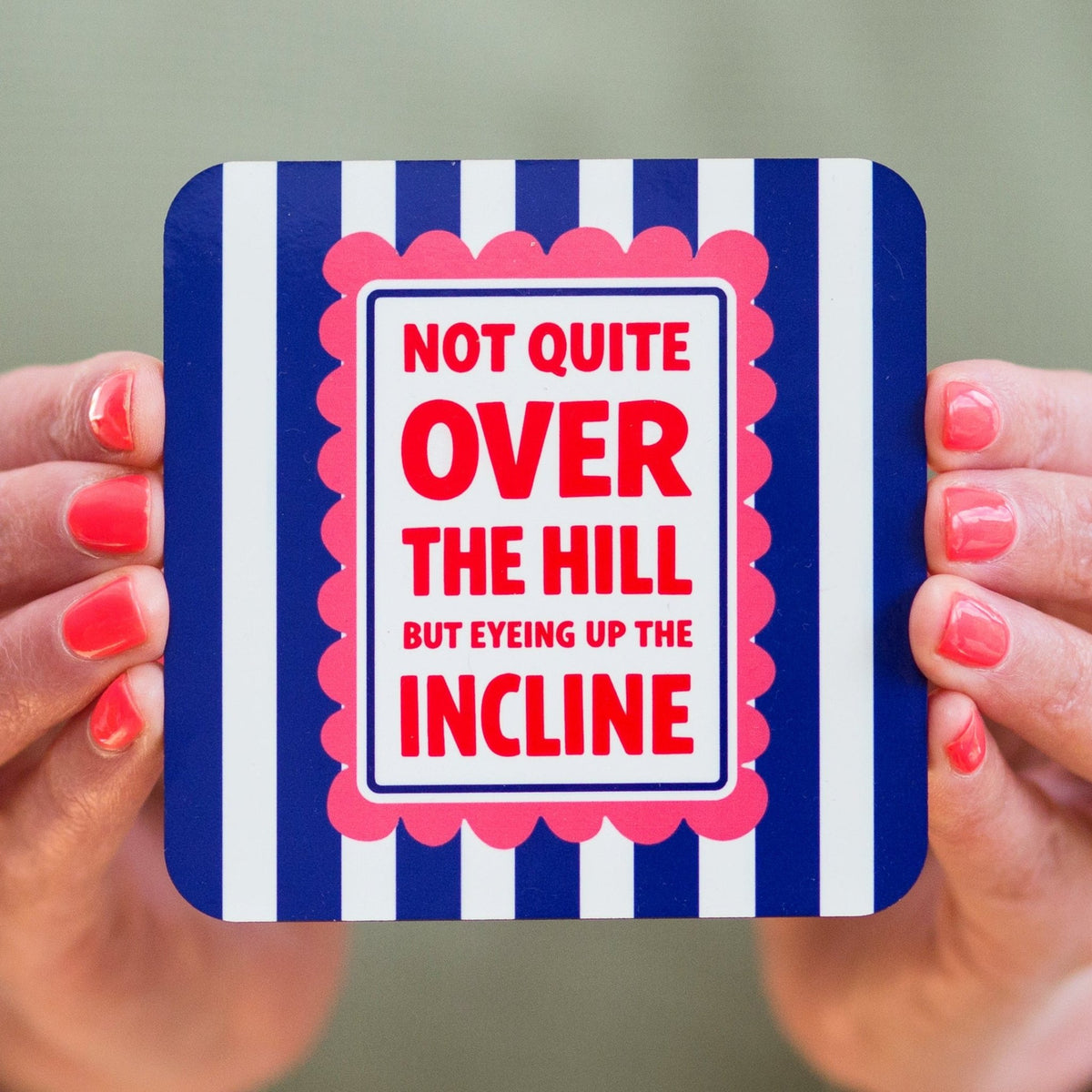 Coaster with humorous text design held by hands against a neutral background