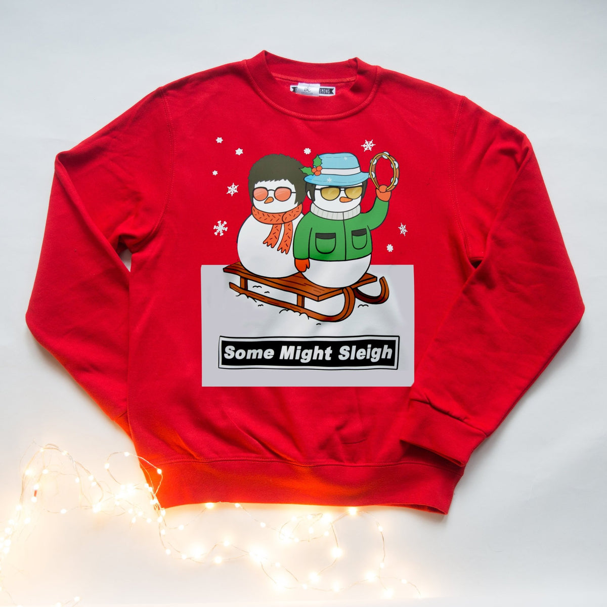a red oasis themed christmas jumper with illustration and some might sleigh pun lying on a white background with christmas lights