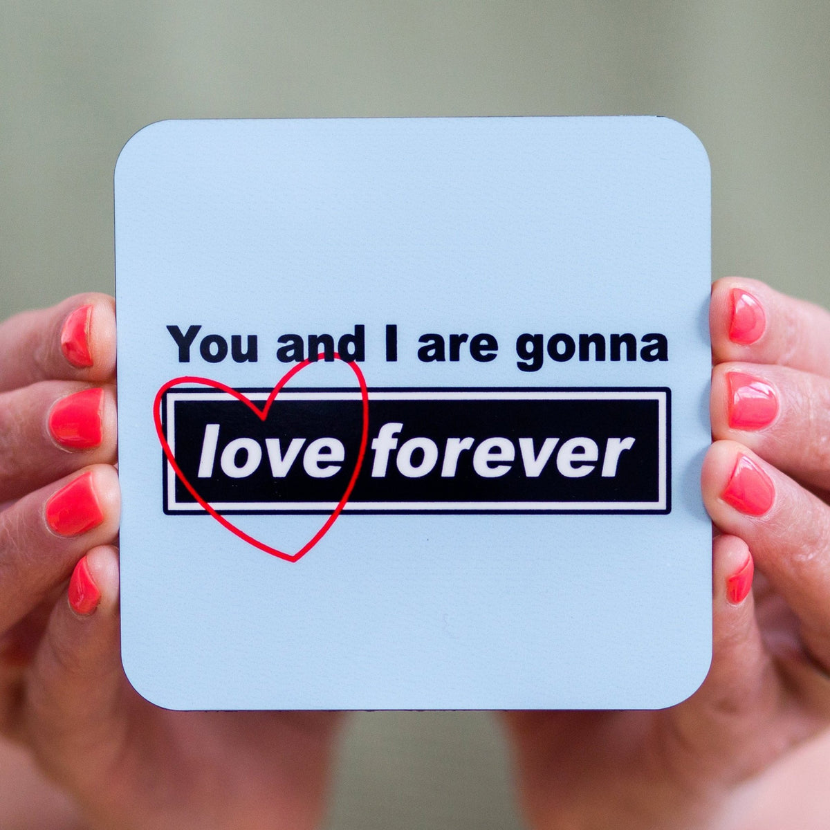 Coaster with 'You and I are gonna love forever' text held by hands with red nail polish.
