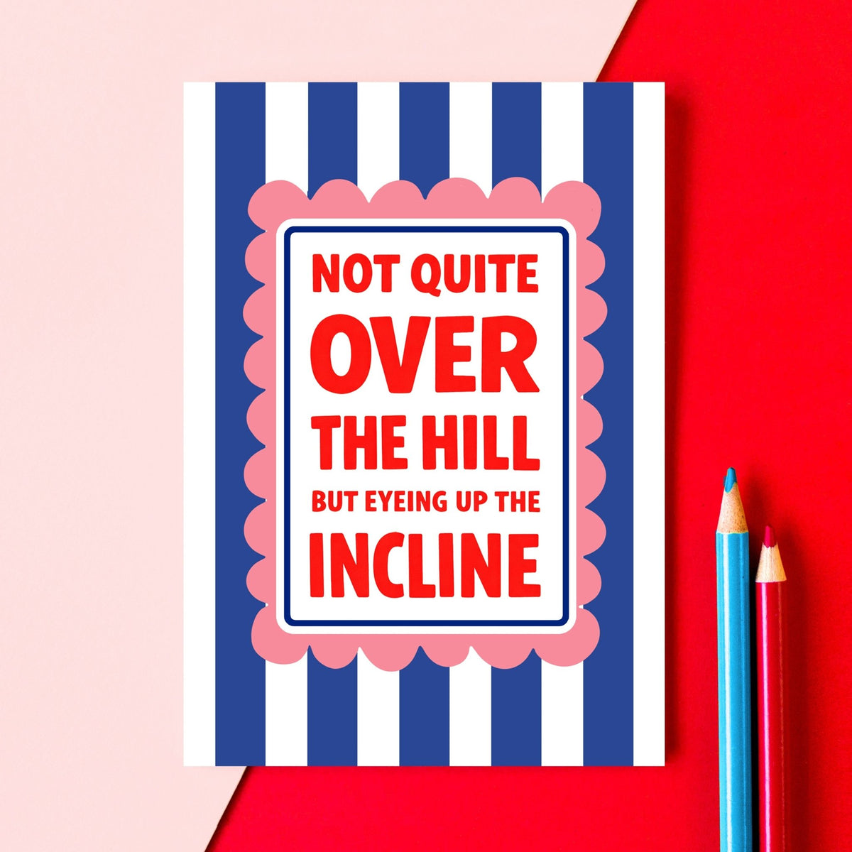 blue and white striped birthday card that says 'not quite over the hill but eyeing up the incline' on a red and pink background