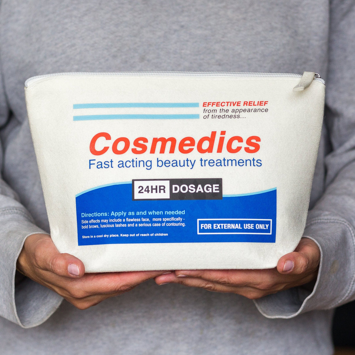parody pill packet cosmetic bag held in hands by female wearing a grey jumper