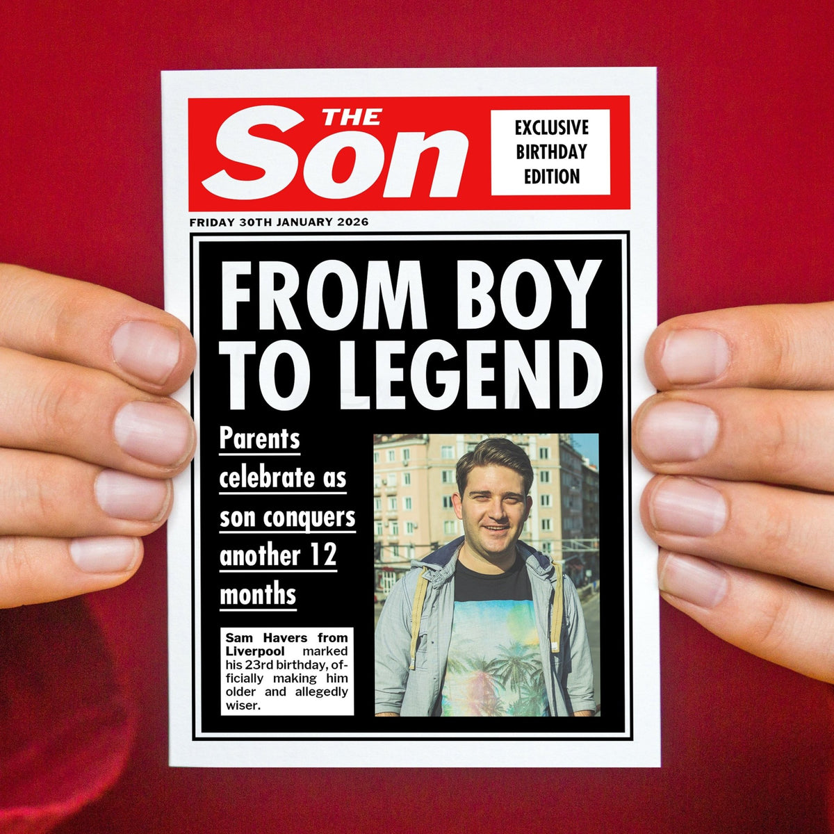 newspaper style custom photo card celebrating a sons birthday, held in hands against a red background