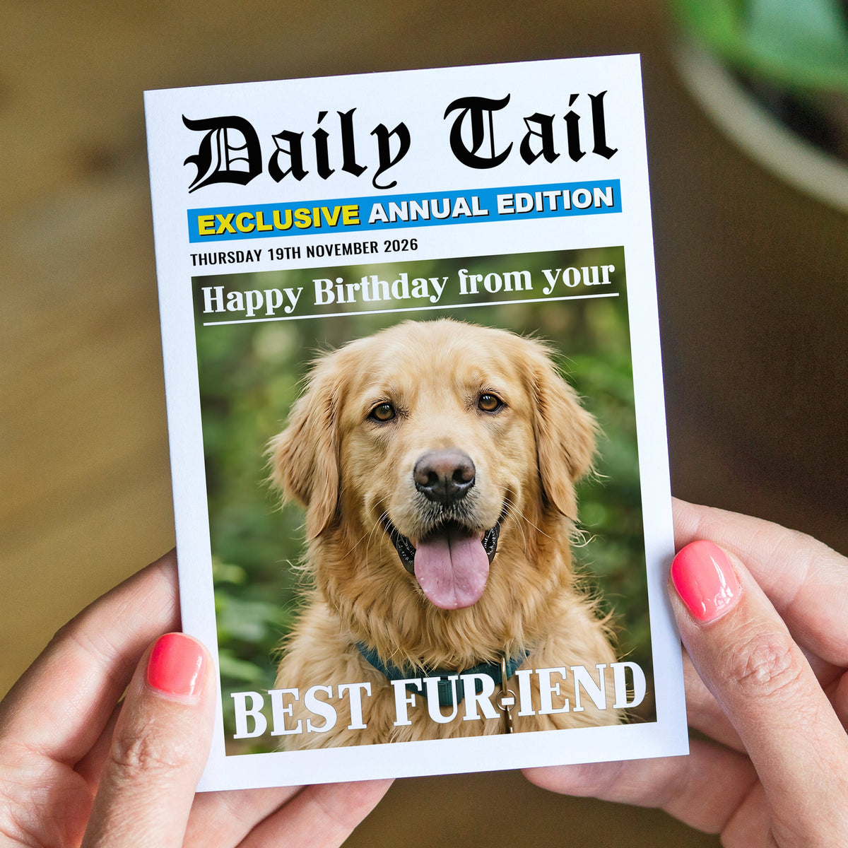 A person holds a printed greeting card styled like a newspaper front page with a photo of a golden retriever and the text 'Daily Tail' and 'Happy Birthday from your BEST FUR-IEND'.