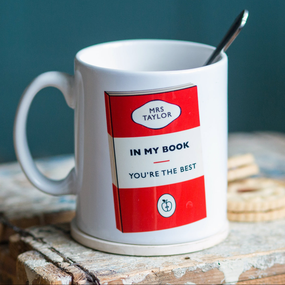 White mug with a red label featuring text and graphics, placed on a wooden surface.