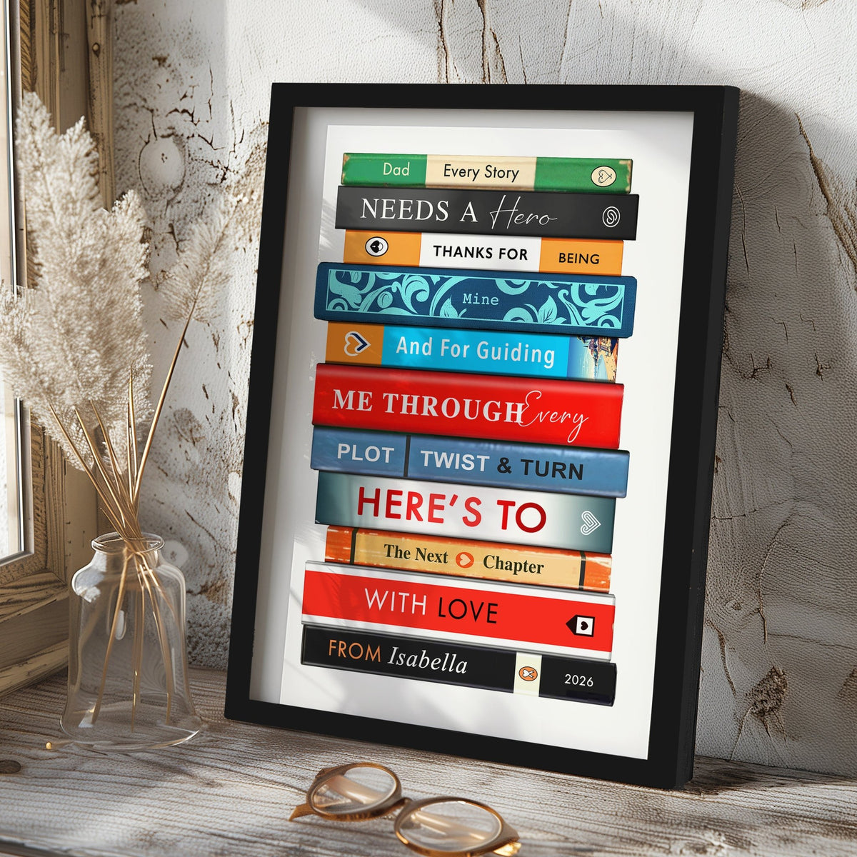 Framed artwork with book design and message for Dad on a wooden surface with a vase and glasses.