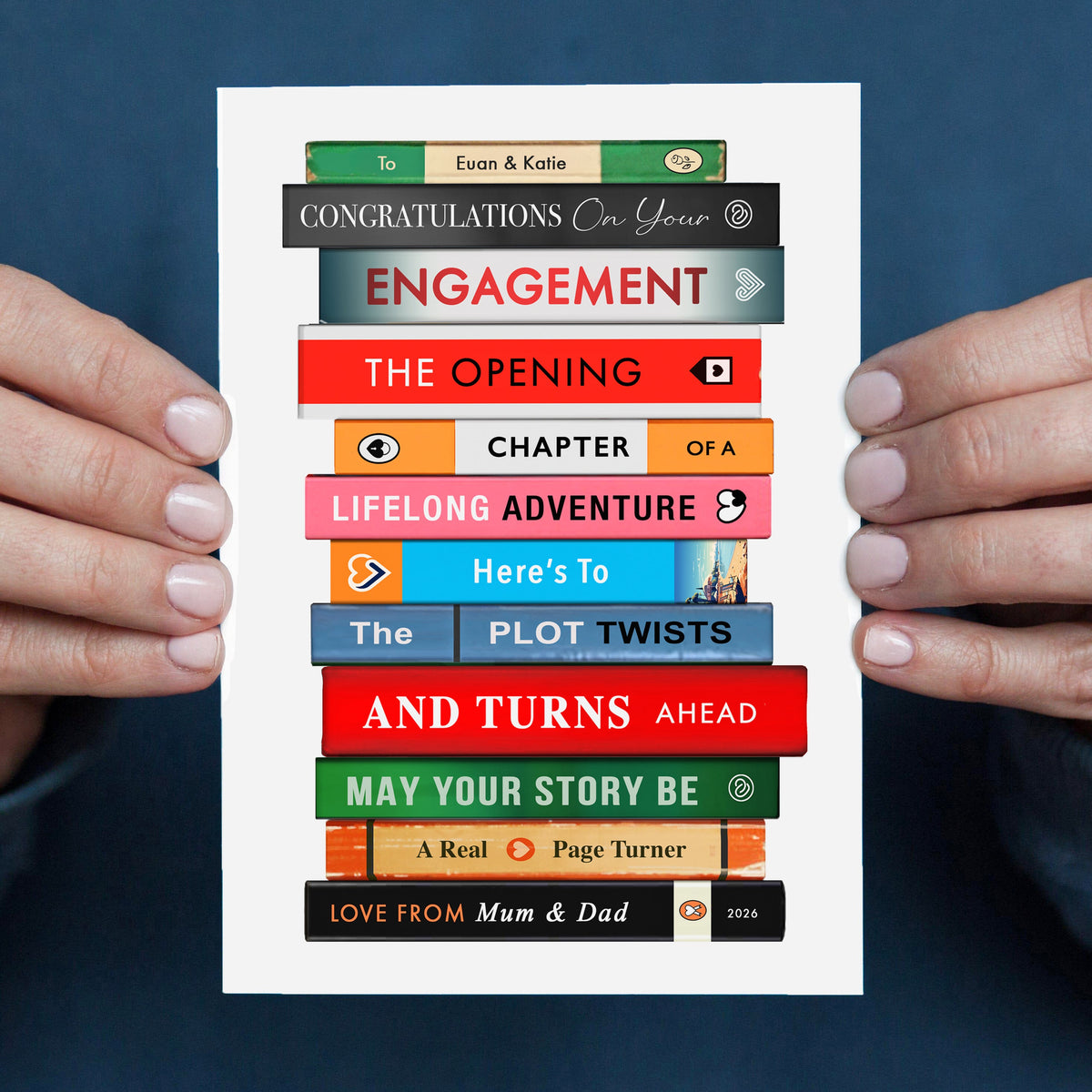 Greeting card with book stack design and congratulations on engagement message held by two hands against a blue background