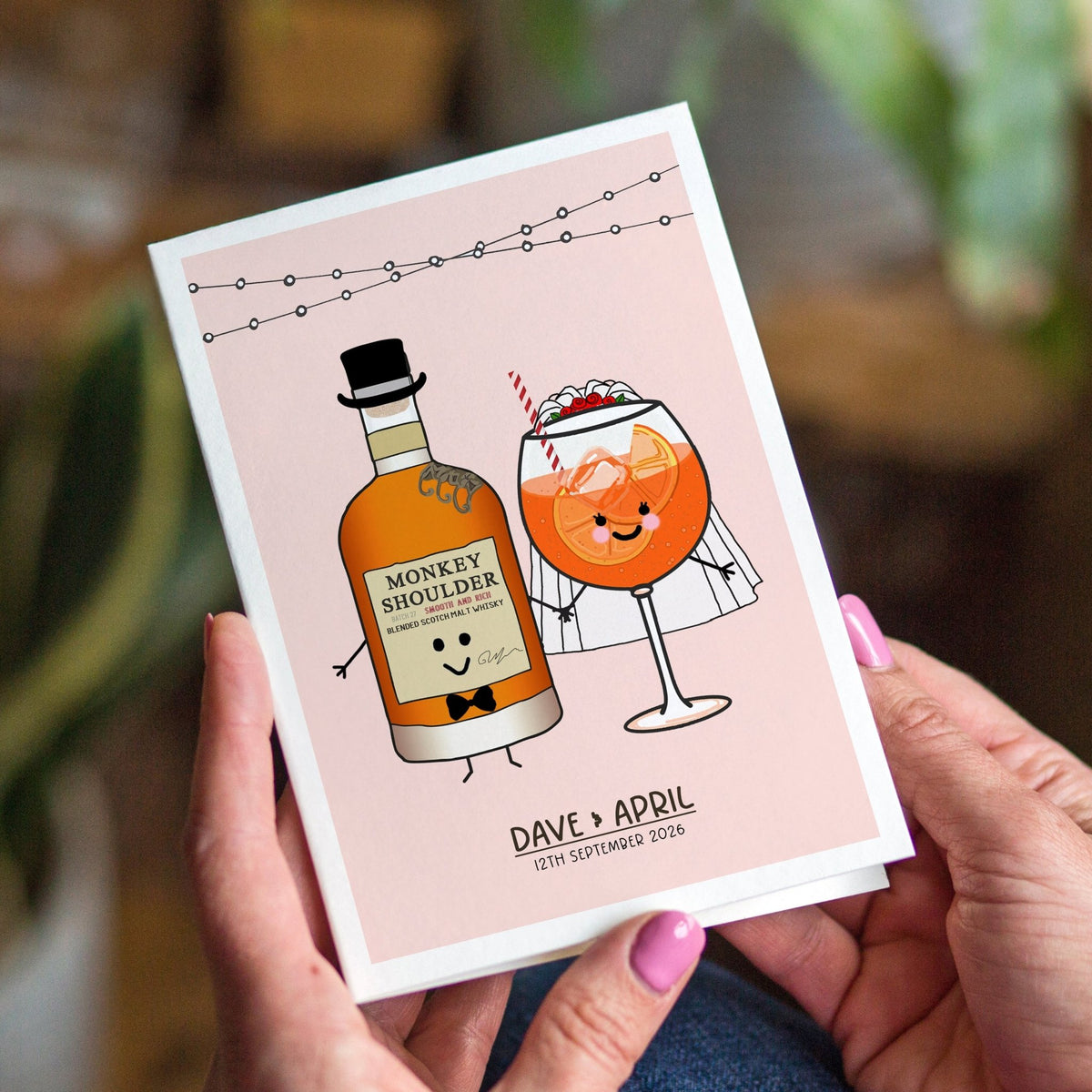Person holding a card with cartoon bottle and glass design, featuring 'Monkey Shoulder' and a cocktail.