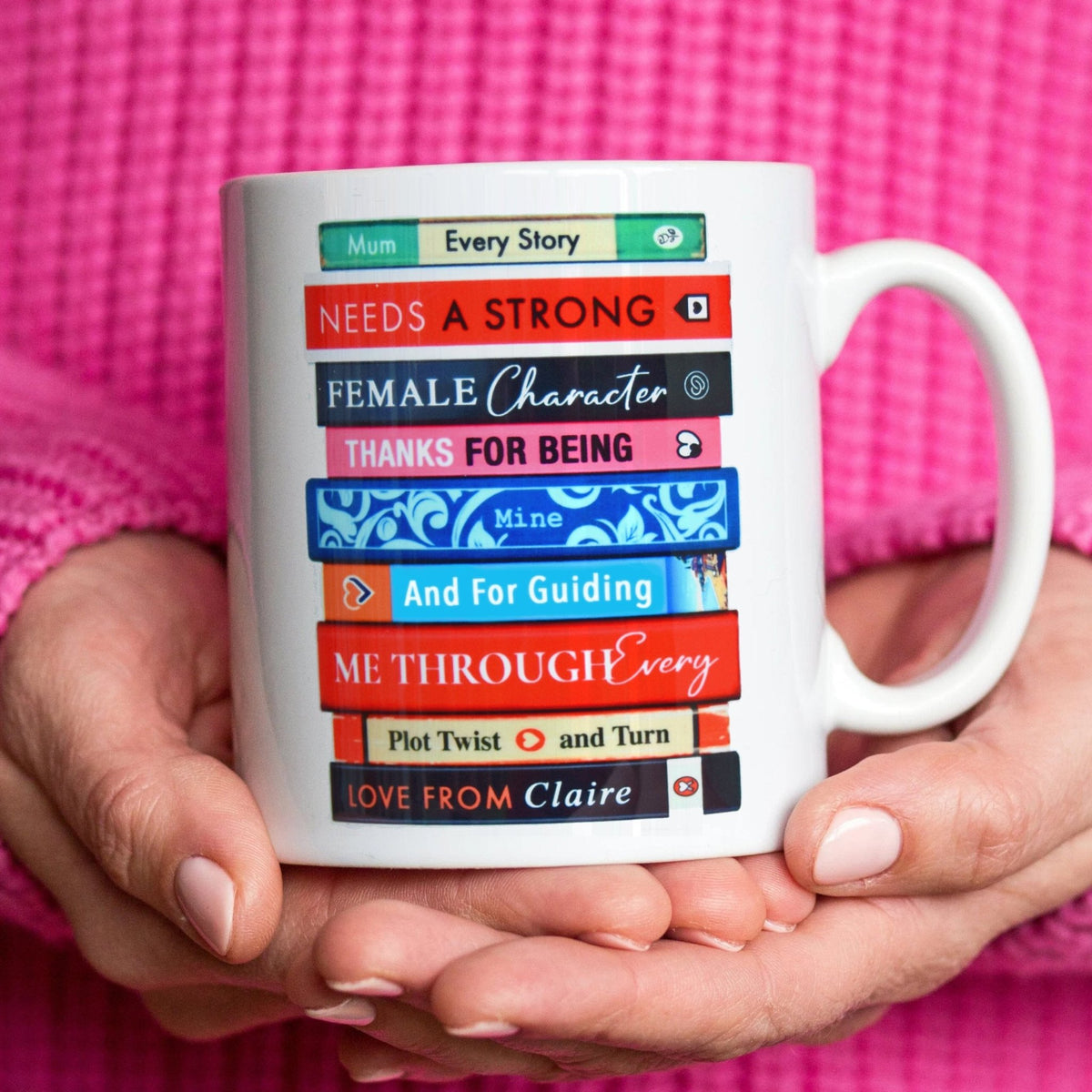 a mug for mums with a book stack design held in female hands against a pink jumper