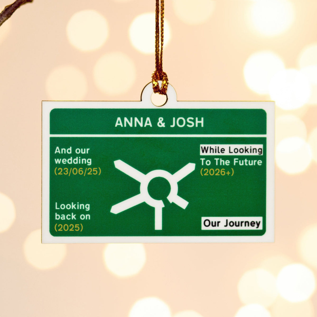 Personalized road sign christmas tree ornament ornament with names Anna & Josh and wedding details on a blurred light background.