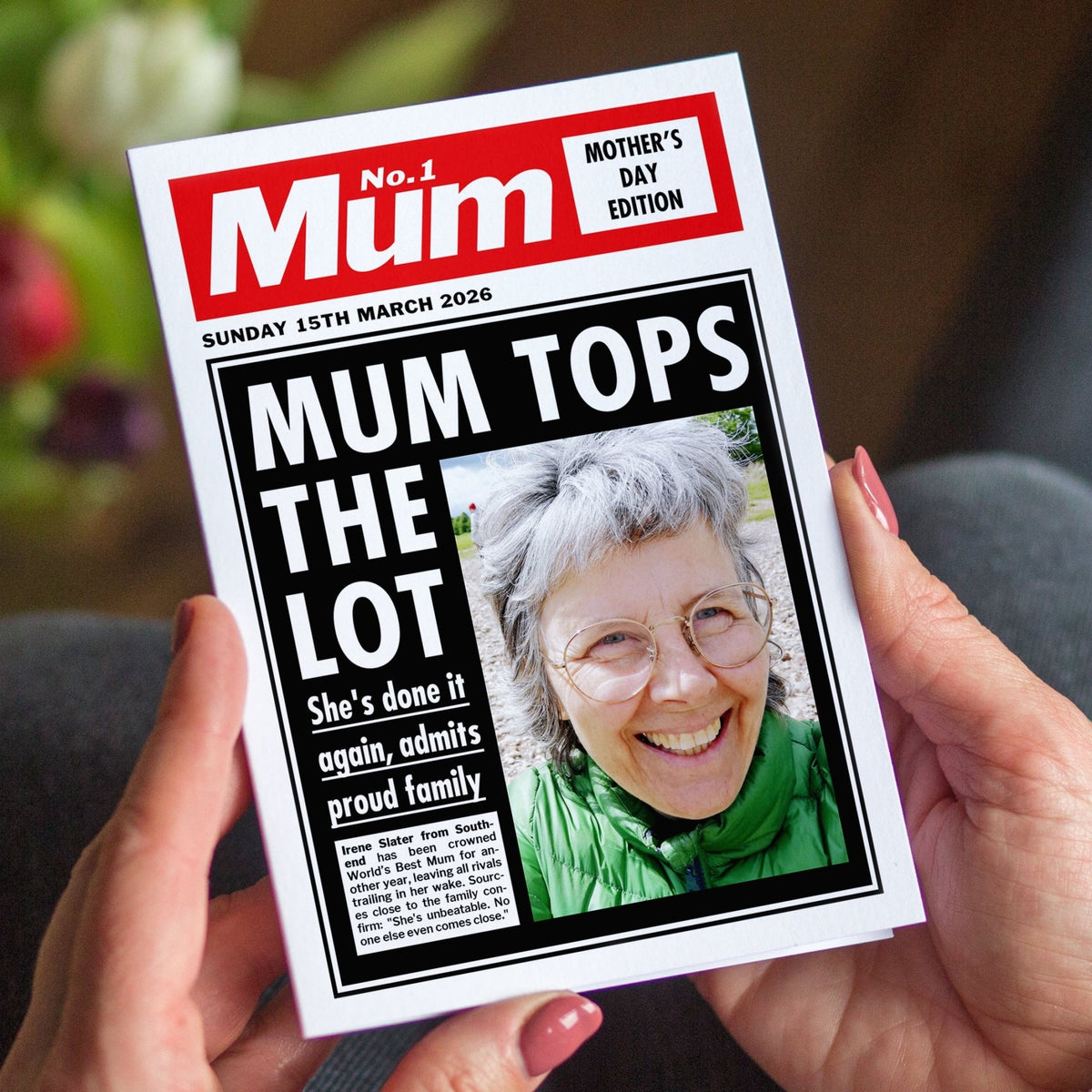 Person holding a Mother's Day card with a front page-style design, featuring text and a photo of a smiling woman.