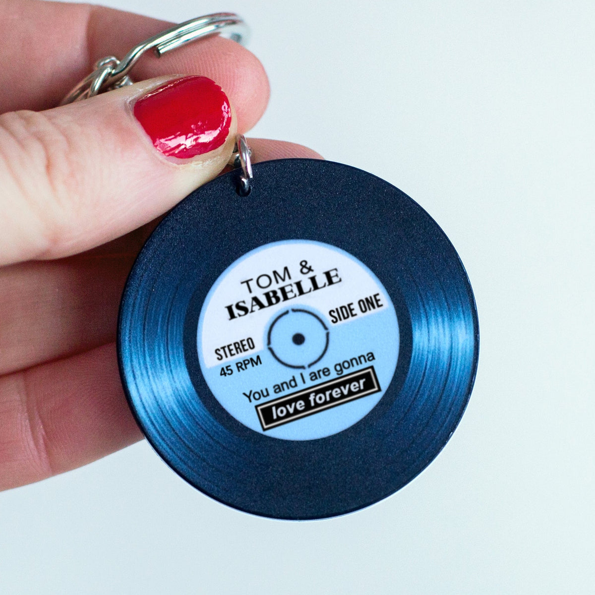 Blue vinyl record keychain with personalized text held by a hand against a light gray background