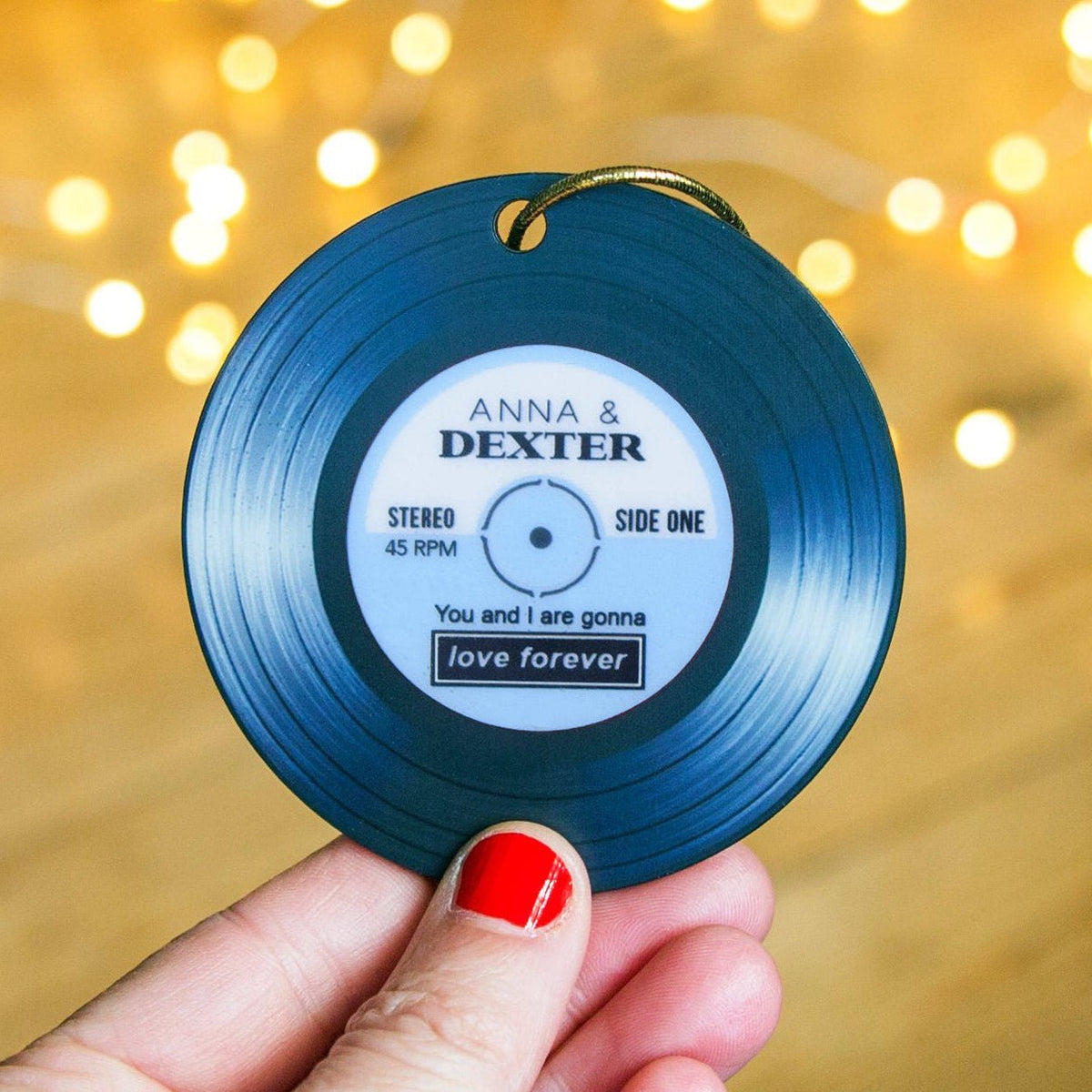 Blue vinyl record ornament with personalized text held against a blurred light background