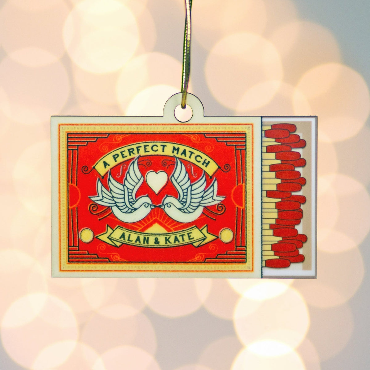 Decorative matchbox ornament with 'A Perfect Match' design and personalized names on a blurred background.