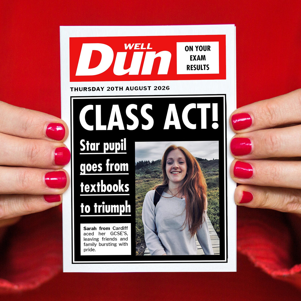 Person holding a greeting card styled like a newspaper with a headline about exam results on a red background