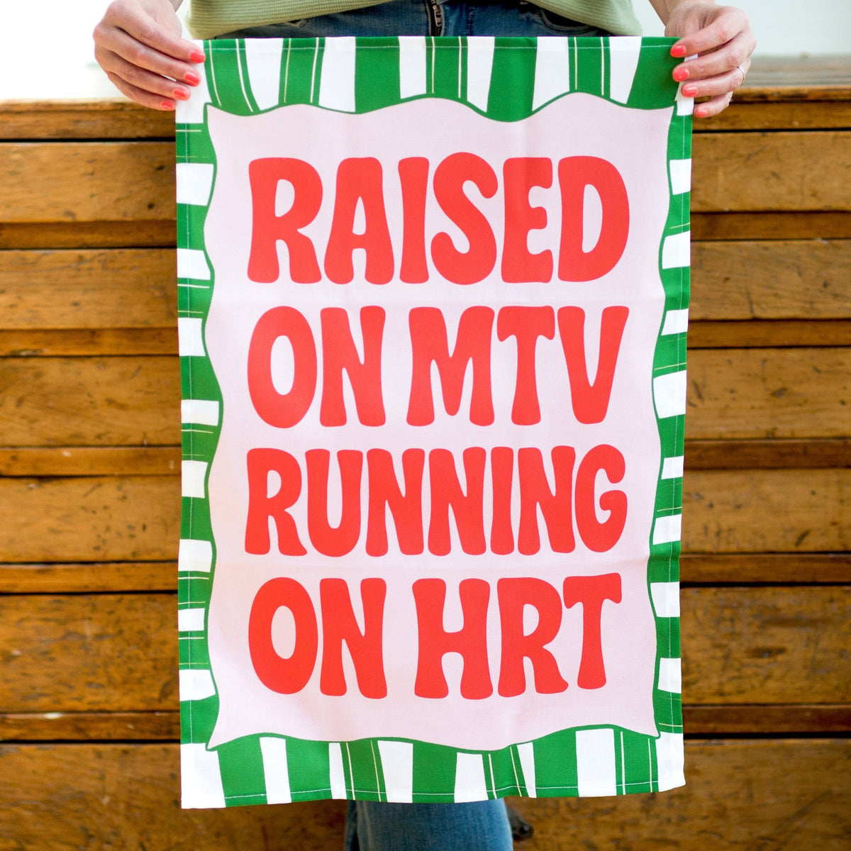 funny tea towel with raised on mtv running on hrt held in hands against a wooden background