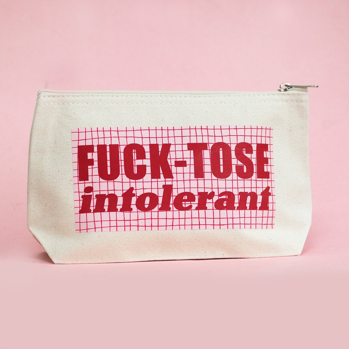 A cream canvas zippered pouch with a red grid pattern and the text 'FUCK-TOSE intolerant' printed on the front, set against a solid pink background.
