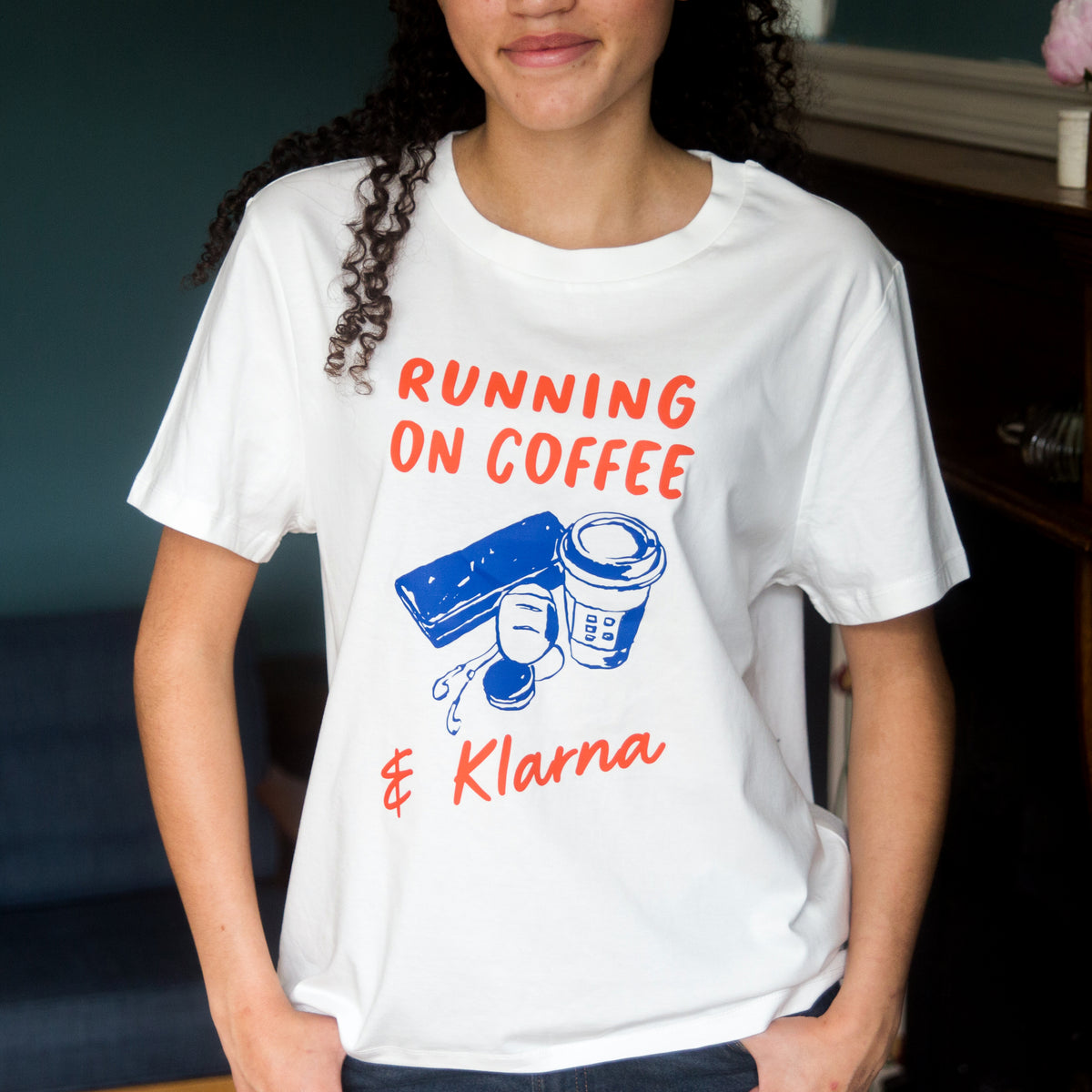 Person wearing a white t-shirt with 'Running on Coffee & Klarna' text and graphics.