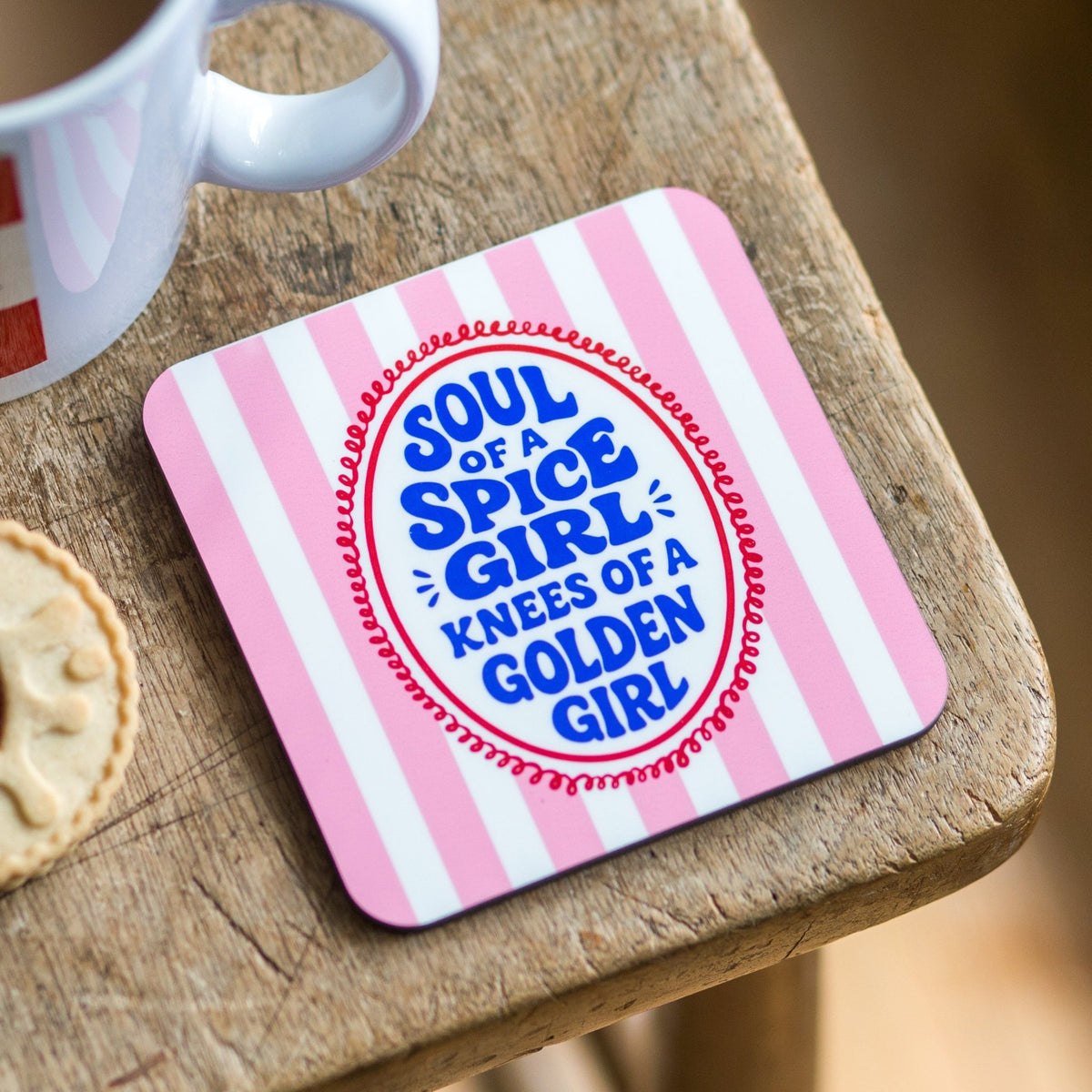 Coaster with 'Soul of a Spice Girl, Knees of a Golden Girl' text on a wooden surface with a mug and cookie.