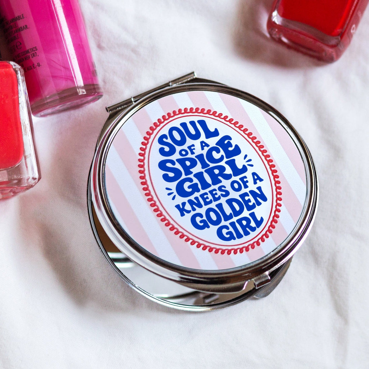 a funny compact mirror for women that has the slogan 'Soul of a Spice Girl, Knees of a Golden girl' surrounded by make up on a white background