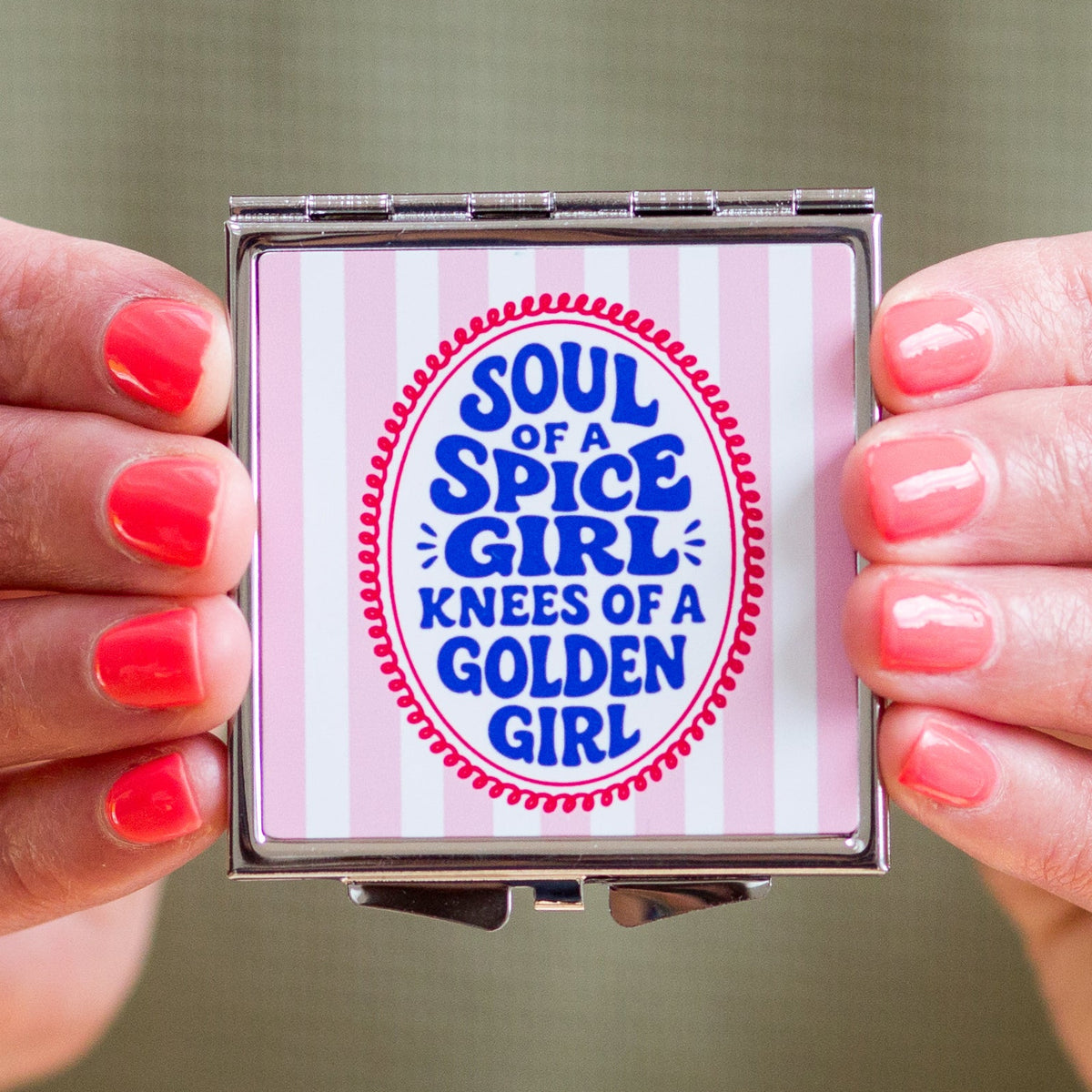 Compact mirror with 'Soul of a Spice Girl, Knees of a Golden Girl' text held by hands with pink nail polish.