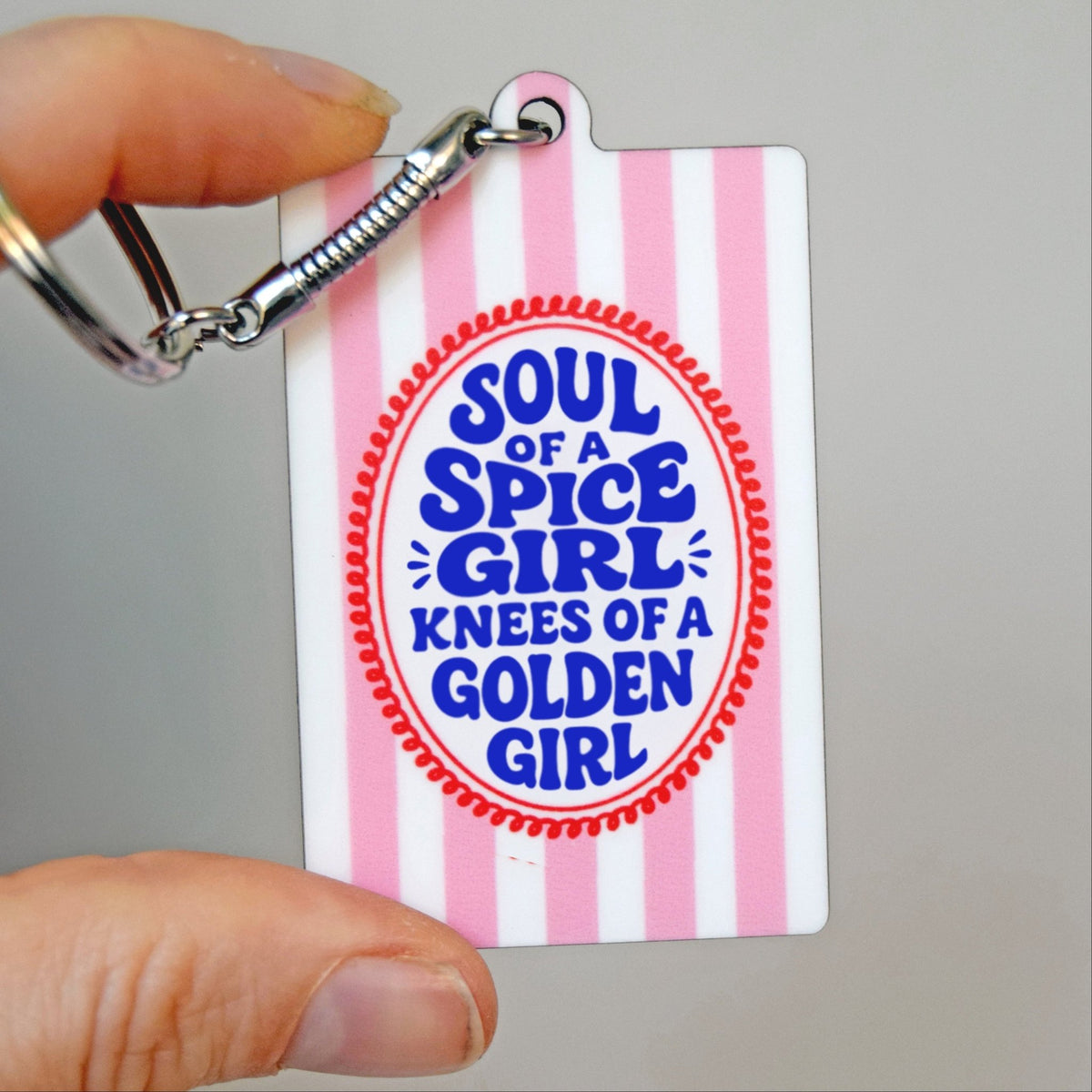 a funny keyring with pink and white stripes and slogan aimed at women held in hand against a grey background
