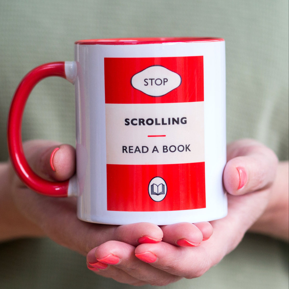 Mug with 'Stop Scrolling Read a Book' text held by hands against a neutral background