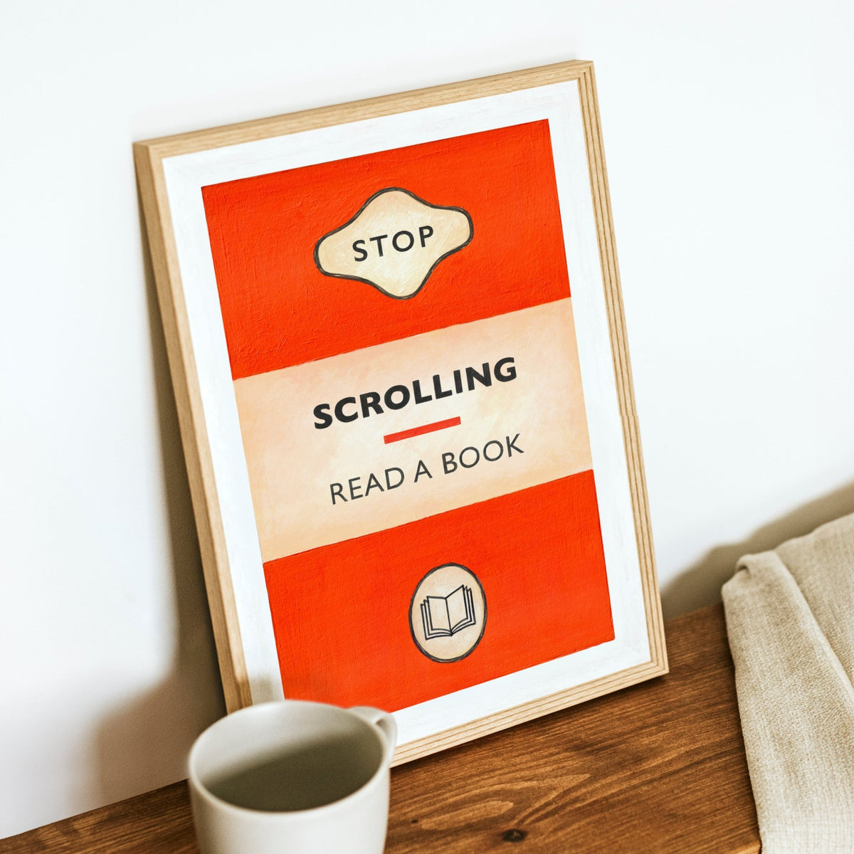 poster designed to look like a book cover that says stop scrolling read a book, in an oak frame on a wooden shelf with mug