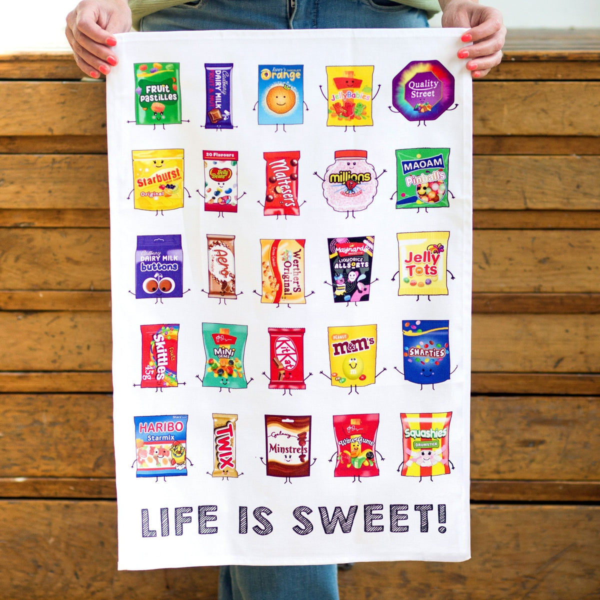 lady holding a tea towel illustrated with different sweets and chocolates against a wooden background