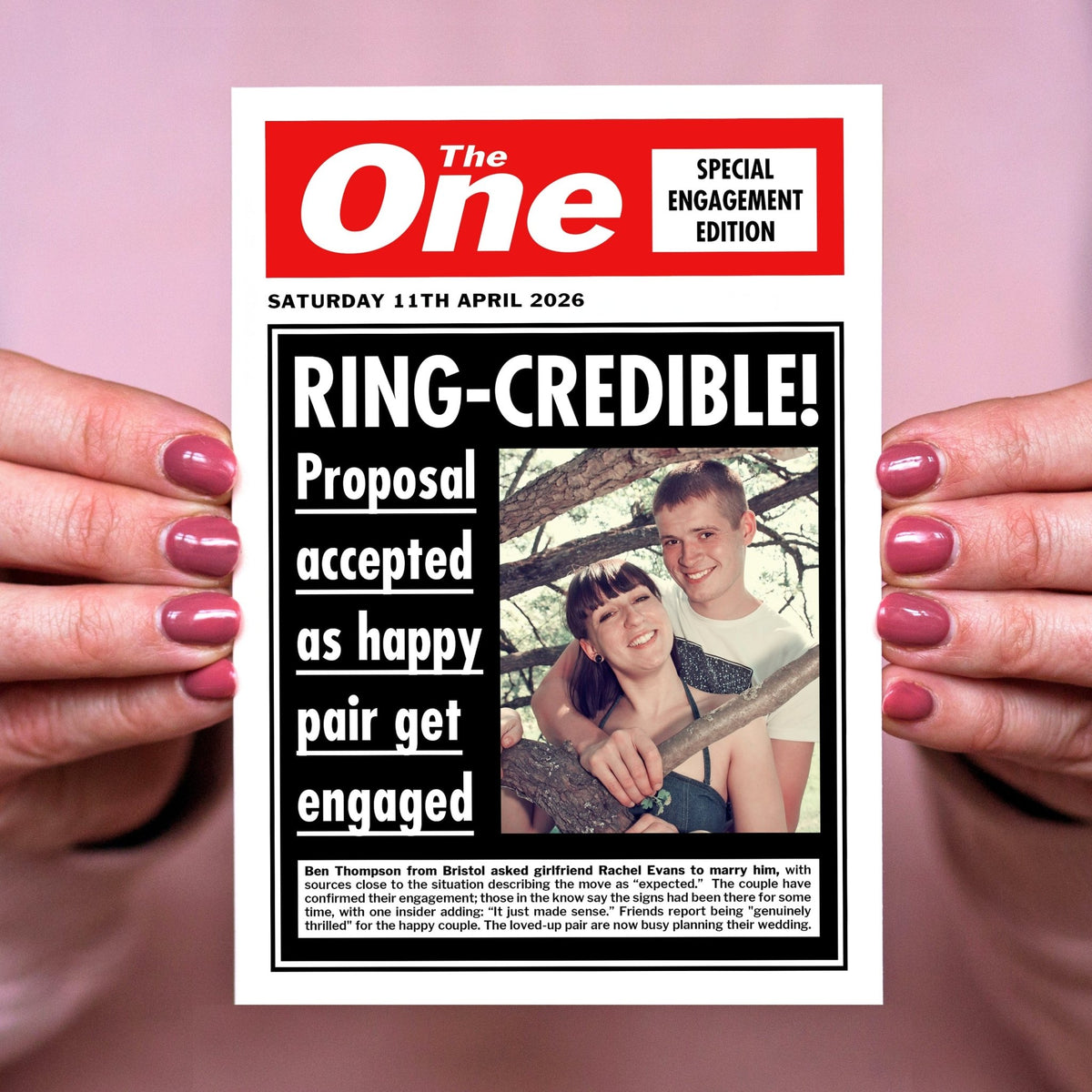 Person holding a newspaper-style card with 'The One' branding and engagement announcement.