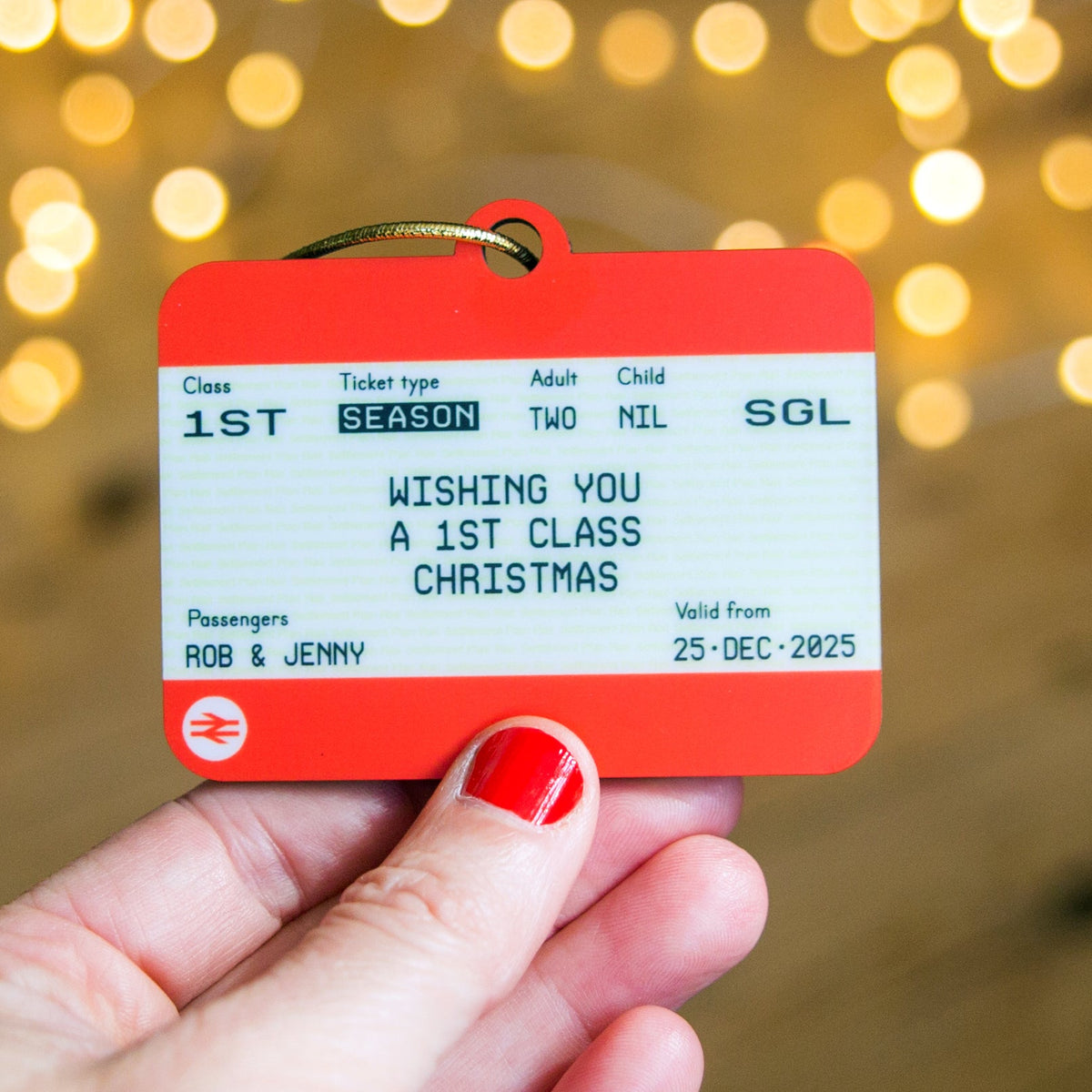 Red and white ticket-style card held by a hand with red nail polish against a blurred festive background.