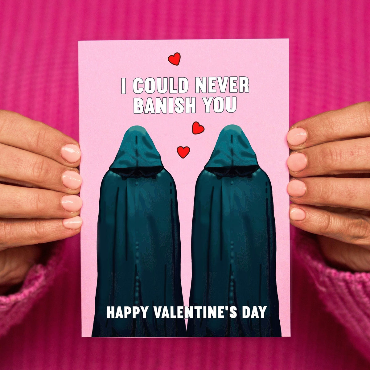 Valentine's Day card with two hooded Traitors  figures and hearts, held by hands against a pink background.