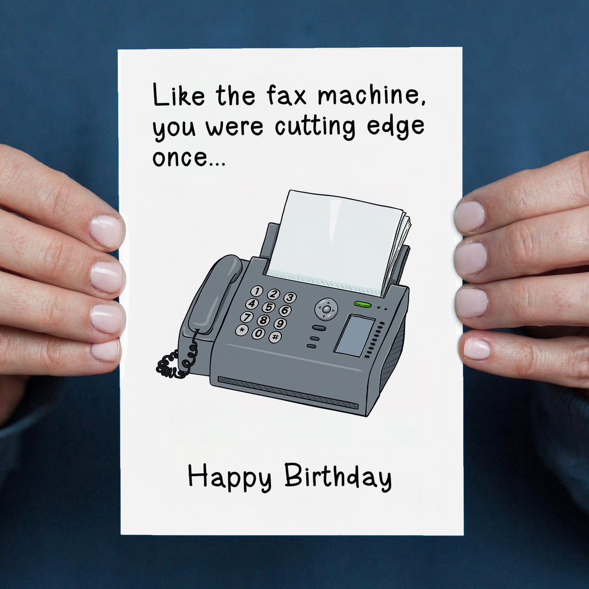 Birthday card with a fax machine illustration and humorous text, held by two hands against a blue background.