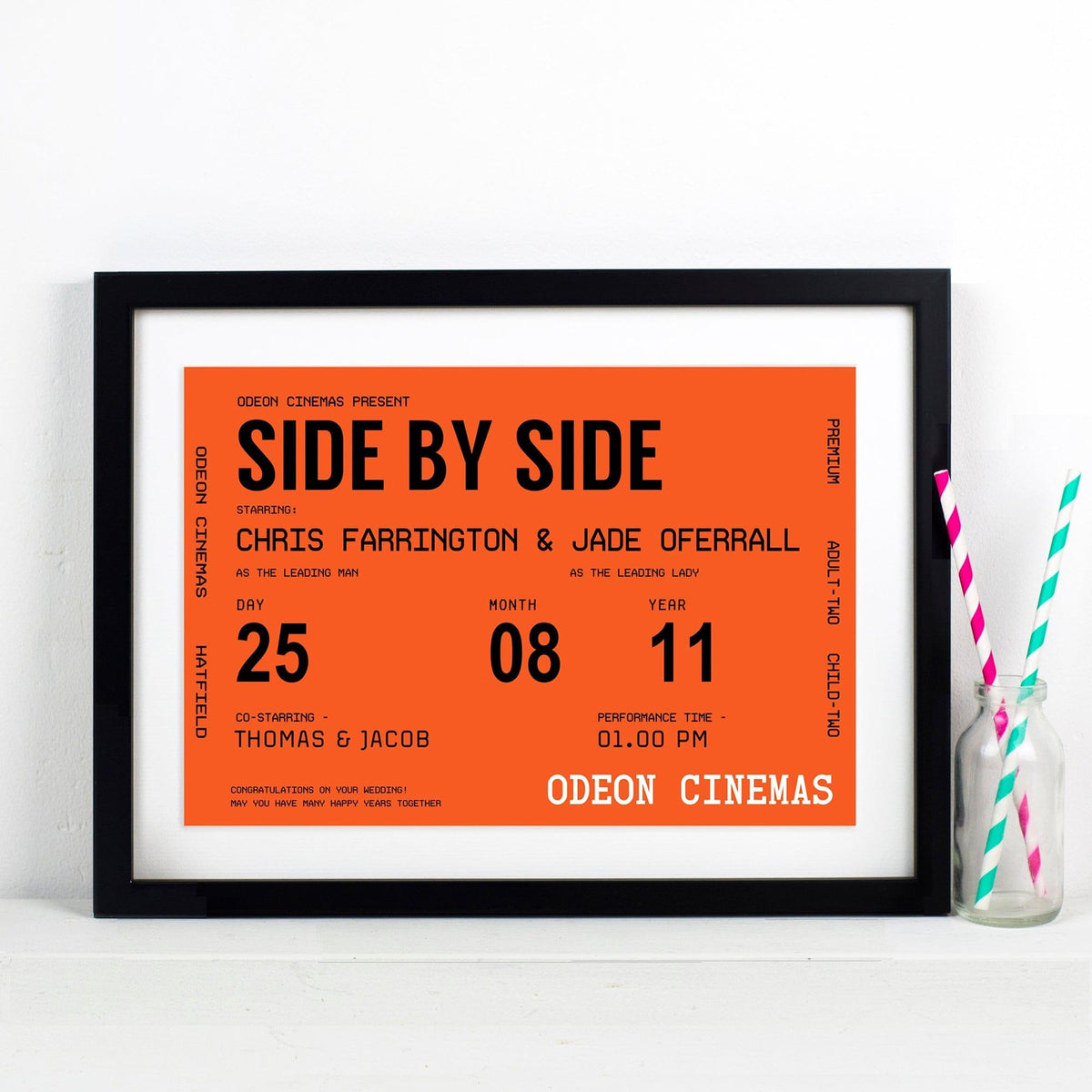 Framed movie poster with 'Side by Side' title and details on an orange background, placed on a white surface with a bottle of water and straws.