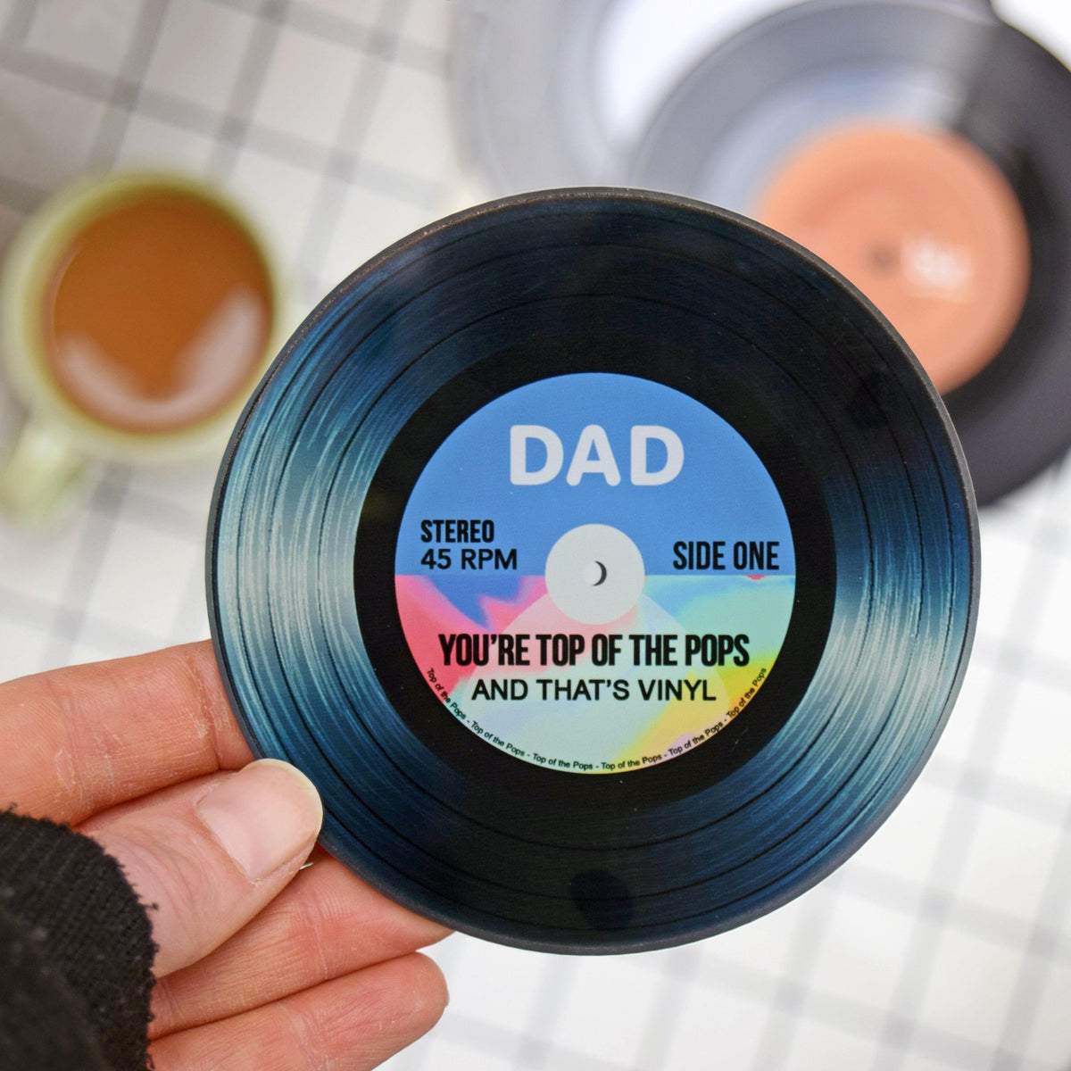 Vinyl record with a personalized label held by a hand, with a blurred background.
